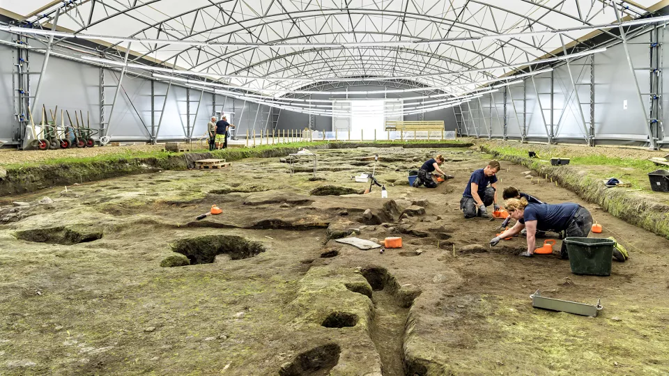 Archaeologists digging in a huge tent. Photo