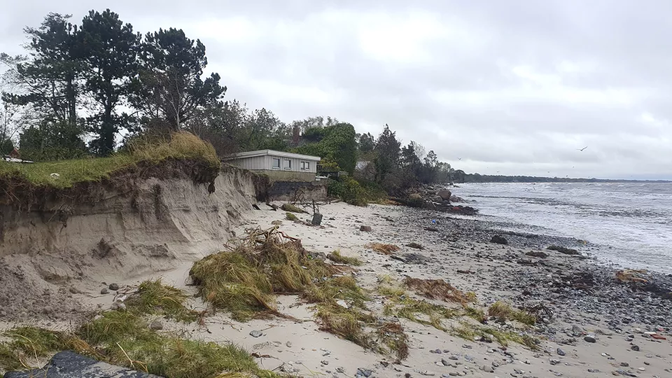 A house on an eroded beach with the sea in the background. Photo