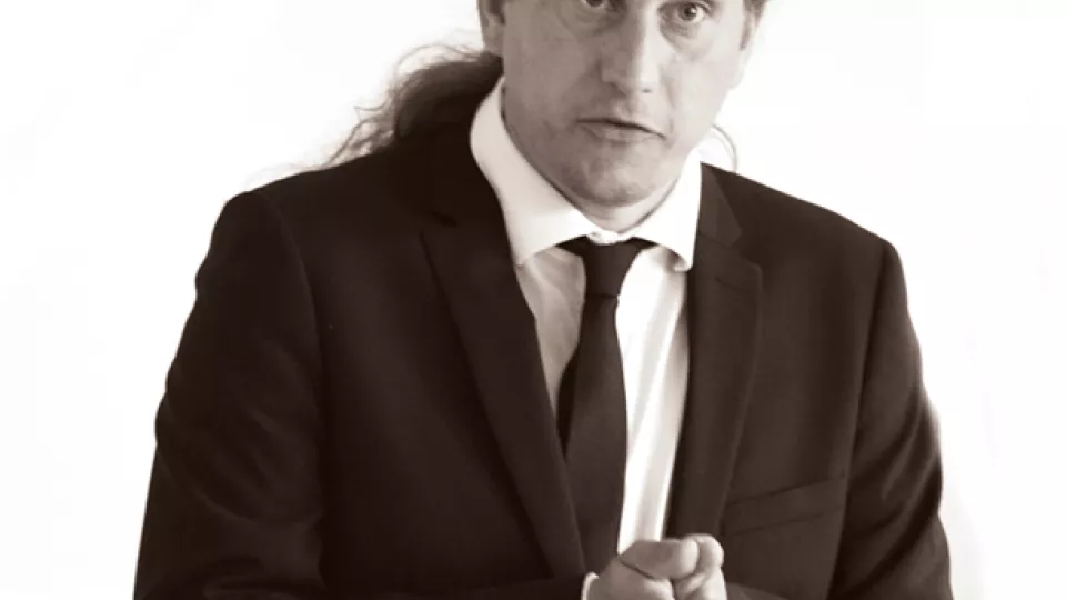 Man in ponytail, black suit and tie 