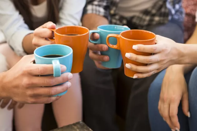 Four persons with cropped heads drinking coffee together.