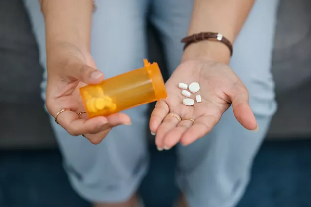 En hand häller upp tabletter ur en pillerburk.