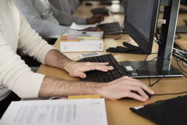 people sitting on a row in front of computers, only hands can be seen.