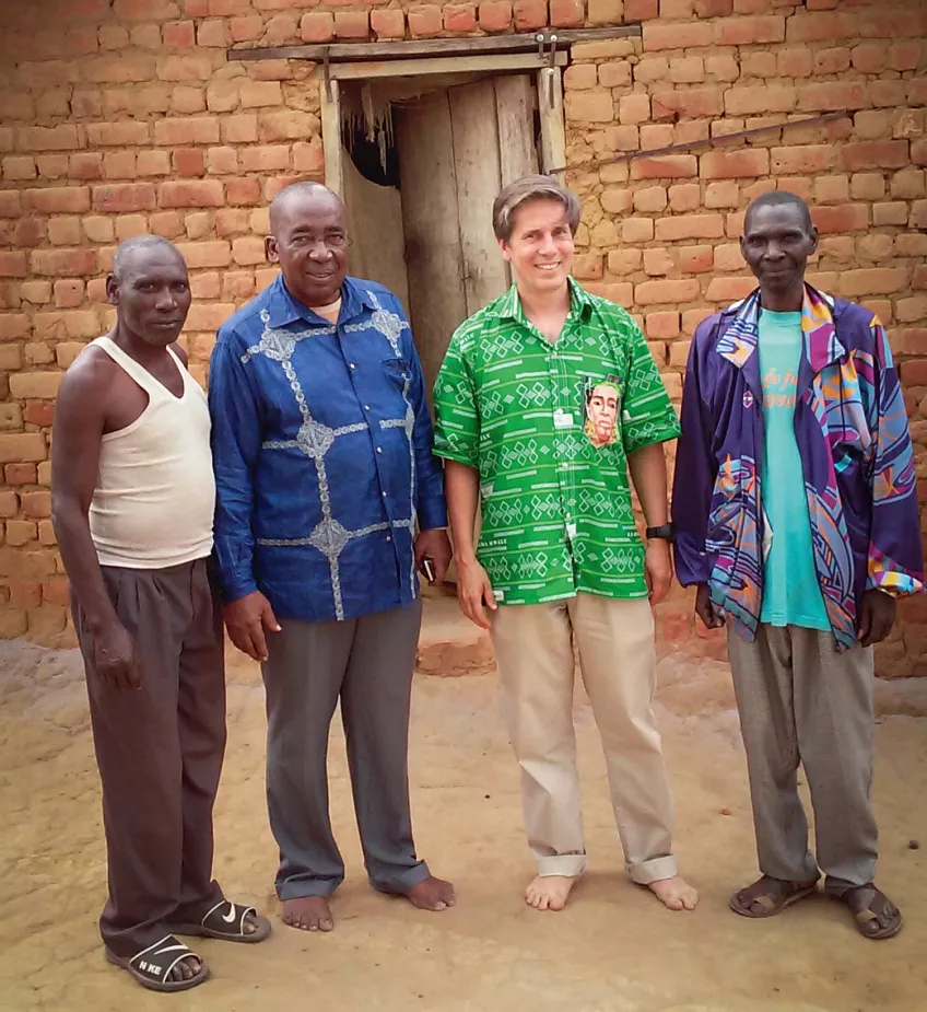 Four men standing barefoot outside a rustic house