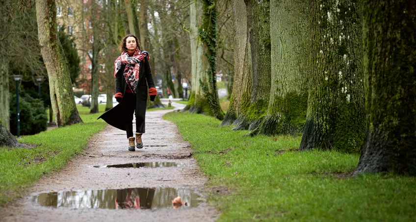 Woman walking in an alley of trees.
