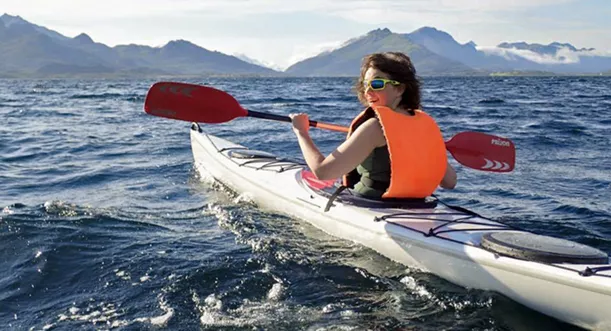 Woman paddling in kayak. Snocapped mountain in the background