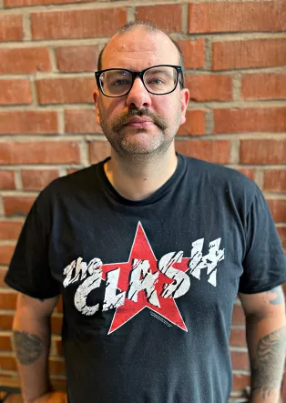 a man with glasses dressed in a The Clash t-shirt. Photo